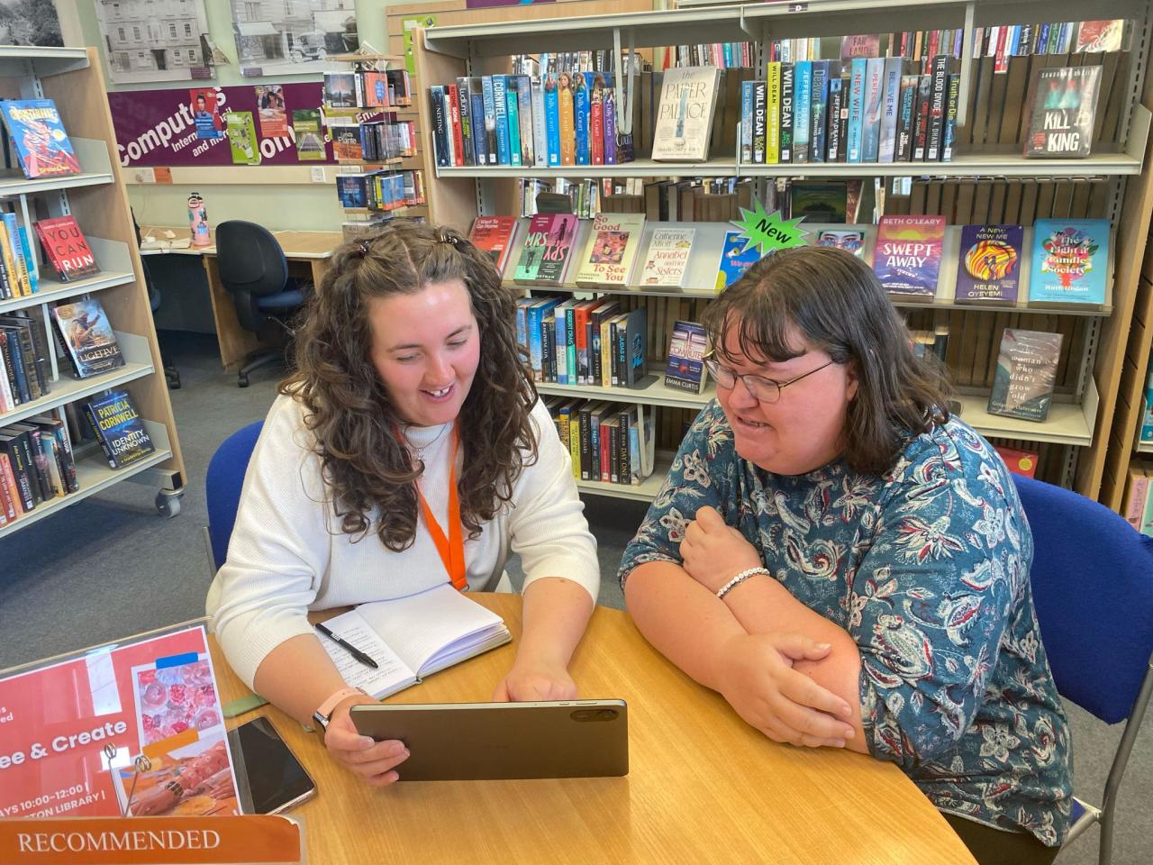 Two people sat in a library setting with an ipad, showing support and advice