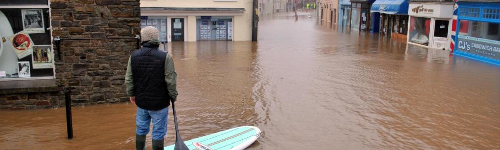 Flooded street in Braunton, Devon, showing a man on a paddle board