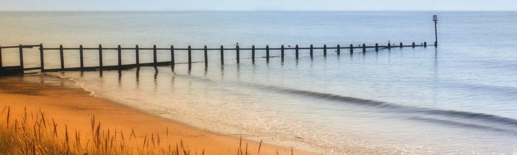 A sandy shoreline with wooden pilings descending into the sea.