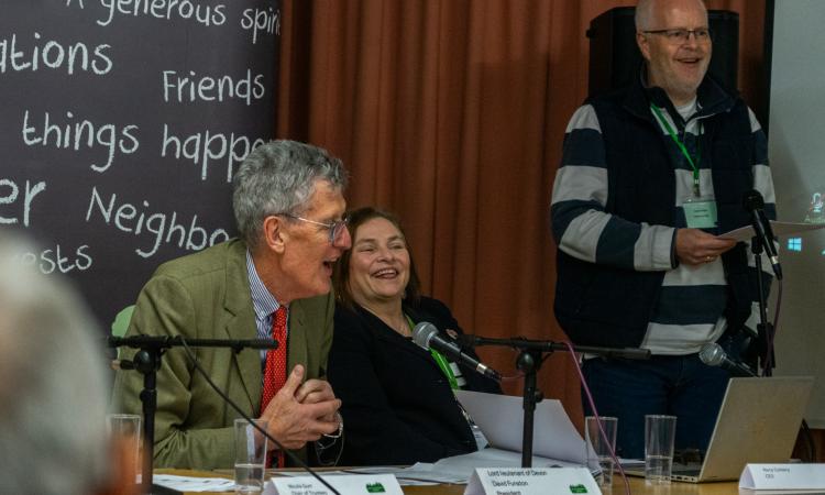 Lord Lieutenant David Fursdon, Nora Corkery and guest speaker sitting at a presentation desk and laughing