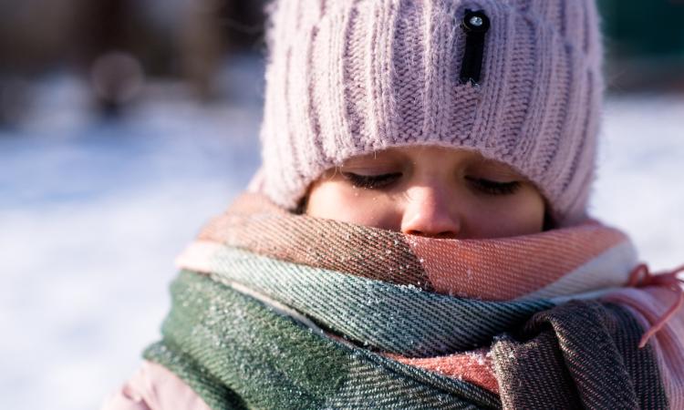 Young girl approximately aged 5 with hat and scarf mostly covering her face. cold snowy background that is blurred. 