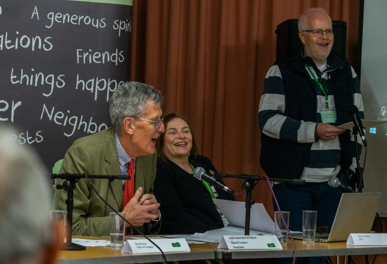 Lord Lieutenant David Fursdon, Nora Corkery and guest speaker sitting at a presentation desk and laughing 