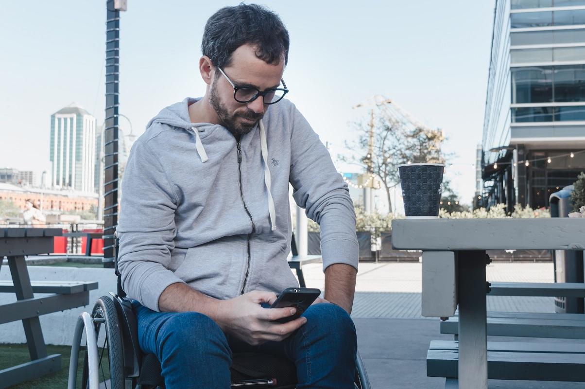 Serious adult male in wheelchair looking down at phone (PIP)